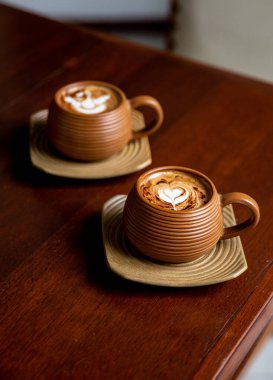 Ahşap masa arkasında iki fincan sıcak kapuçino. Aşkın sembolü olarak kalp şeklinde latte sanatı. Sabah rutini için bir fincan..