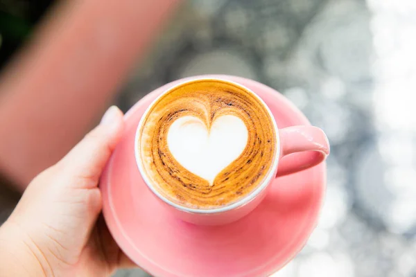 在大理石桌子的背景上 有时髦的粉色热卡布奇诺杯 心形拿铁艺术作为爱情的象征 每天早上喝一杯 免版税图库图片