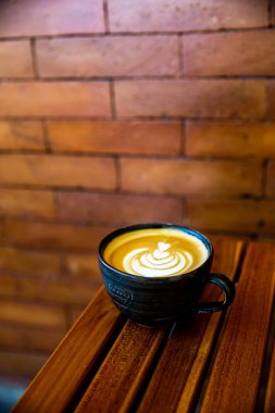 Ahşap arka planda latte sanatıyla kapuçino. Güzel köpük, ahşap masa ve tuğla duvar. metin için yer