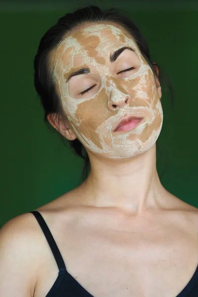 Νεαρή μελαχρινή γυναίκα με μια πήλινη σπιτική μάσκα στο πρόσωπό της με τα μάτια κλειστά — Φωτογραφία Αρχείου
