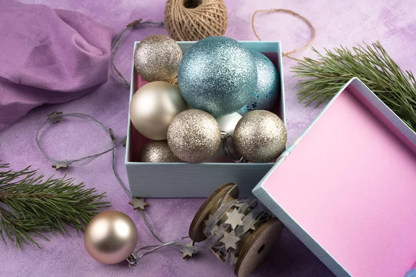Різдвяні кульки в синій коробці з кришкою та гілками сосни на рожевому фоні . — стокове фото