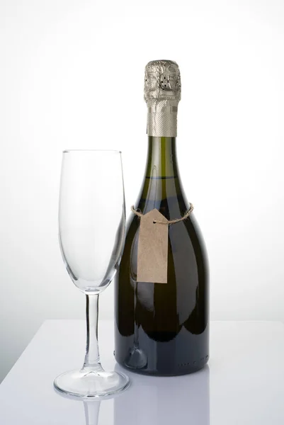 Una botella de alcohol con una etiqueta en una cuerda y un vaso sobre un fondo claro. — Foto de Stock