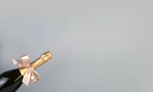 Uma garrafa de champanhe com um arco em um fundo cinza. — Fotografia de Stock