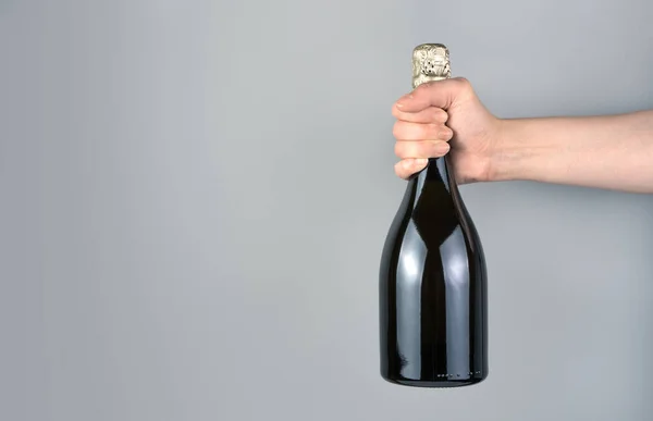 A bottle of sparkling wine in the hand of a woman on a gray background.