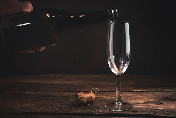 Mano sosteniendo una botella de champán sobre una copa vacía sobre un fondo oscuro. — Foto de Stock