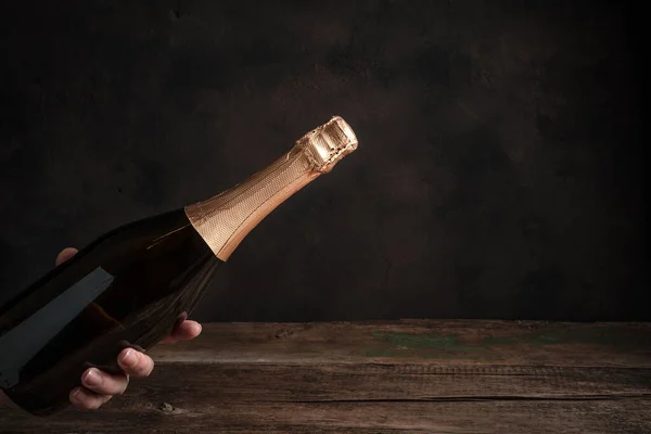 Uma garrafa de champanhe sem rótulo na mão de uma mulher em um fundo de madeira. — Fotografia de Stock
