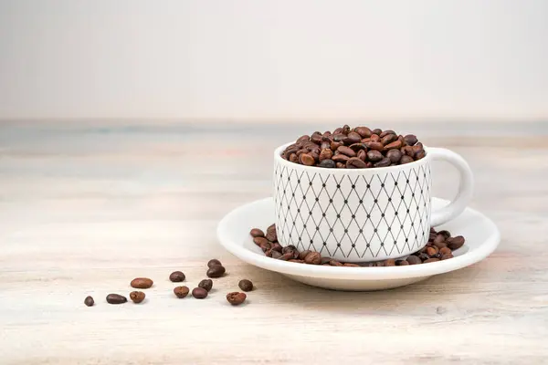 Latar belakang kopi, biji kopi dituangkan ke dalam cangkir dengan latar belakang cahaya. — Stok Foto