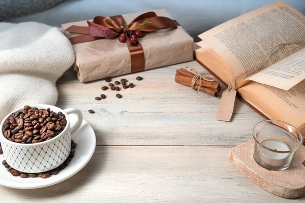 A mug with coffee beans, a gift box, a book, a sweater on a wooden table, with space for copying. — Stock Photo, Image