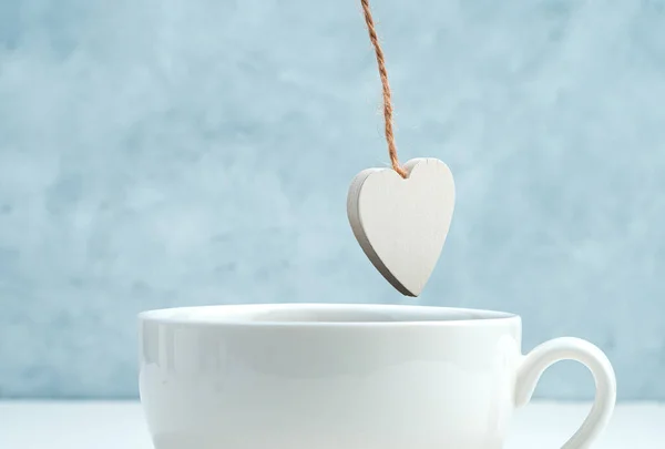 A wooden white heart hangs over a Cup of coffee. — Stock Photo, Image