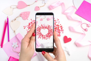 Bir kadının elleri telefonu romantik bir arkaplanda tutar..