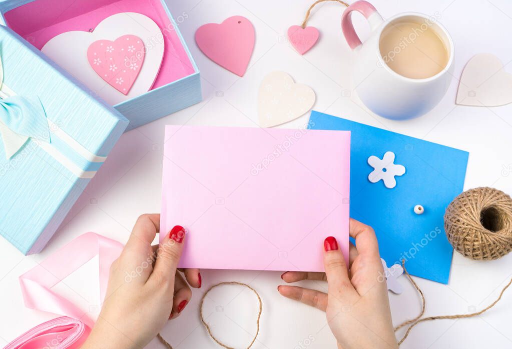 A womans hands hold a pink envelope on a romantic background in pink and blue colors.