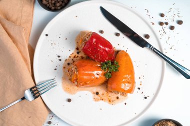 Açık arkaplanda maydanoz ve baharatla süslenmiş kırmızı ve turuncu biberli mutfak kompozisyonu.