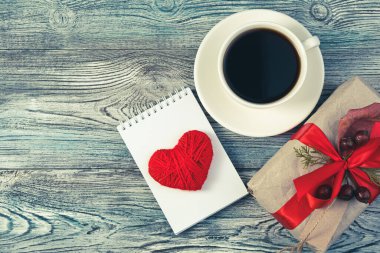 Hediye kutusu, kalbi olan bir not defteri ve gri-mavi ahşap arka planda bir fincan kahve..