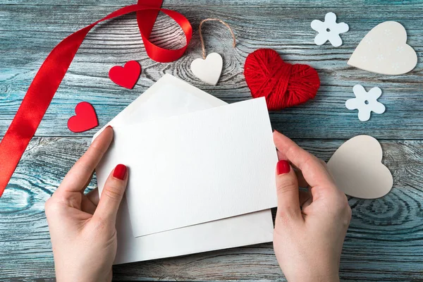 Uma mulher segura um envelope branco com uma carta vazia em um fundo romântico com corações e uma fita. — Fotografia de Stock