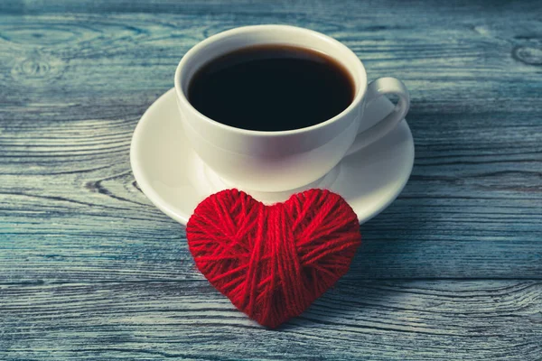 A large red heart is leaning against a coffee mug on a saucer. — Stock Photo, Image