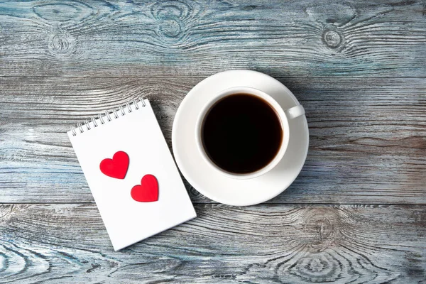 White coffee mug and two red hearts on a Notepad on a wooden background. — Stock Photo, Image