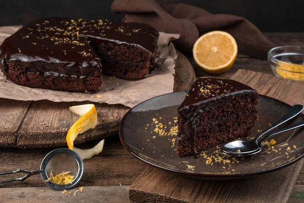 茶色の木の背景にアイシングとレモンゼストのチョコレートケーキ. — ストック写真