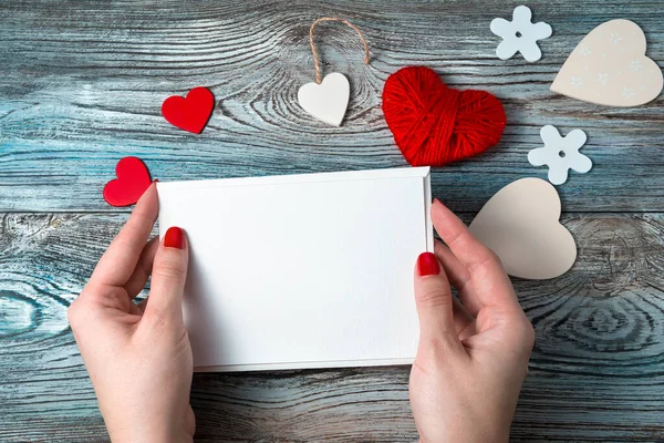 Envelope branco com uma carta vazia nas mãos de uma mulher em um fundo romântico com corações e uma fita. — Fotografia de Stock