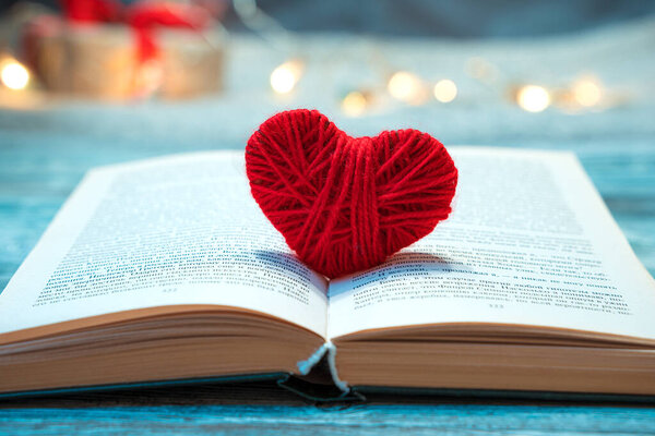 An open book with a red heart on the background of a burning garland.