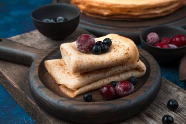 Donmuş kirazlar ve Rowan, mavi arka planda, ahşap bir tabakta krep..