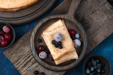 Koyu mavi arka planda kızarmış krep ve donmuş böğürtlen ile mutfak arka planı.