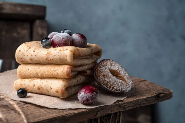 Delicious pancakes with frozen cherries, plums and mountain ash on a wooden tray.