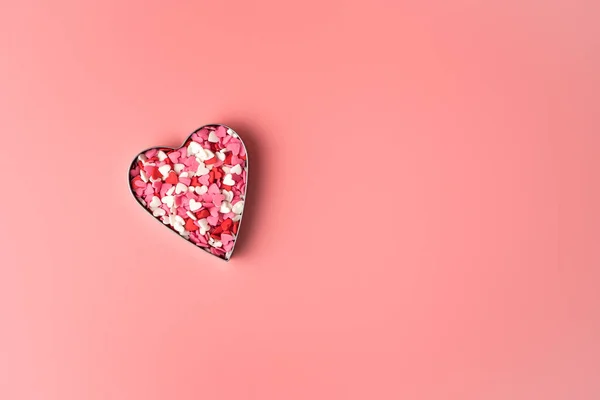 Metal heart filled with confetti in the shape of hearts on a pink background. Royalty Free Stock Photos