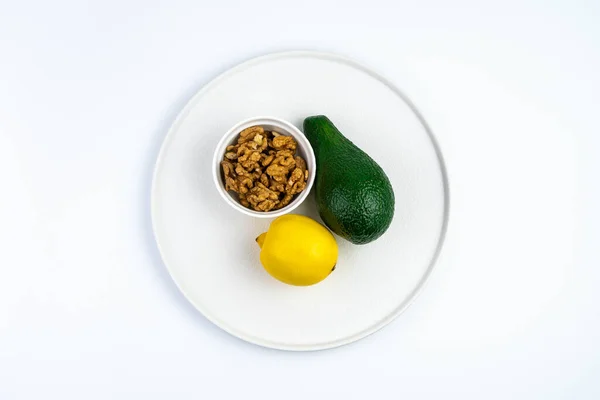 白い平皿にアボカドとレモンとクルミ。コピーするスペースのあるトップビュー. — ストック写真