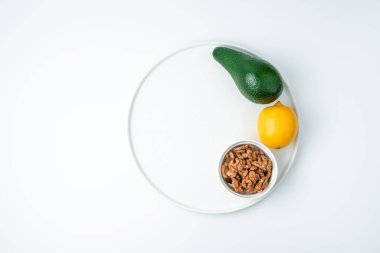 Avokado, limon ve ceviz beyaz arka planda bir tabakta.
