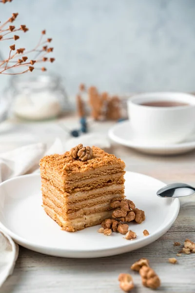 A piece of honey cake with nuts on a light background. Side view.