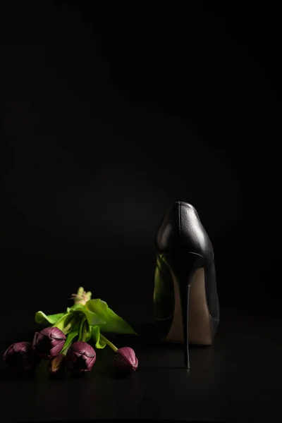 Womens high-heeled shoes and a bouquet of tulips on a black background.