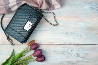 Hafif ahşap bir arka planda çanta, eşarp ve çiçekler. Kopyalamak için boşluk olan üst görünüm.