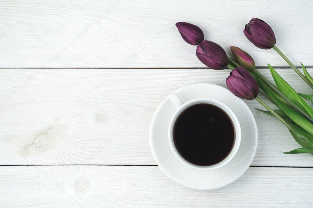 A cup of coffee on a saucer and a bouquet of tulips on a light wooden background. Top view, with space to copy.