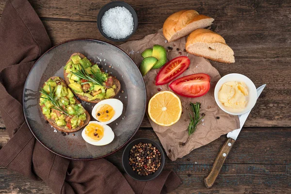 Almuerzo con tostadas con guacamole y romero, huevos cocidos, tomates y limón sobre fondo de madera. — Foto de Stock