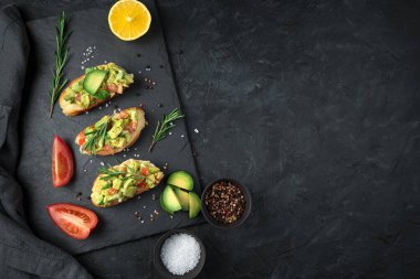 Kızarmış tost, limon, biberiye ve domatesli siyah çimento üzerine guacamole..