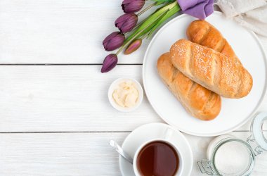 Taze ekmek, tereyağı, bir buket lale ve ahşap zemin üzerinde çay..