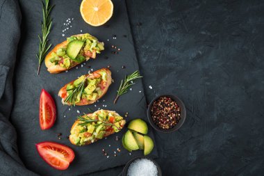 Üç taze guacamole sandviç ve domatesler siyah beton bir masada düz tabakta.