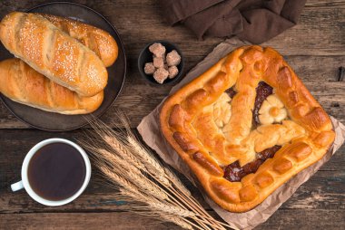 Elmalı turta, taze ekmek ve buğday dikenleri ve kahverengi ahşap arka planda bir fincan çay..