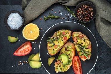 Ekmek üstü avokado, domates ve siyah arka planda limon..
