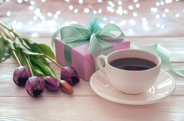 Fondo festivo con una taza de café, flores y envases de regalo en el fondo de una guirnalda en llamas. —  Fotos de Stock