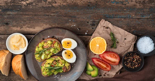 Завтрак с бутербродами с авокадо, помидорами, лимоном, маслом на деревянном фоне. — стоковое фото