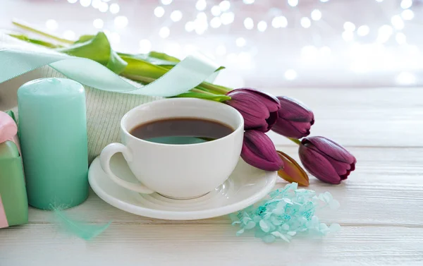 A cup of coffee, candles, flowers on a light background with a burning garland.