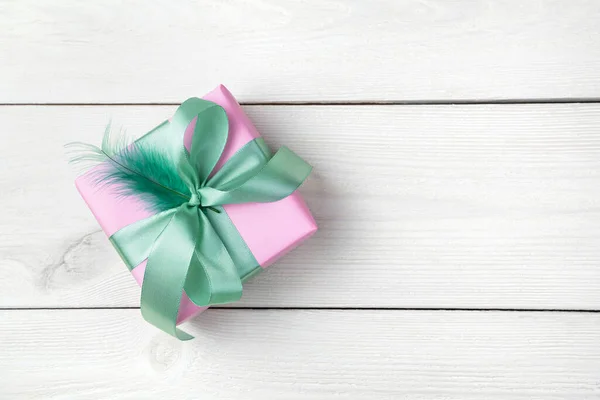 Una caja de regalo decorada con una cinta de color menta y plumas sobre un fondo de madera blanco. —  Fotos de Stock