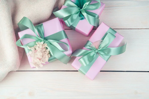 Tres cajas de regalo rosas con cintas y un suéter sobre un fondo de madera blanco. —  Fotos de Stock