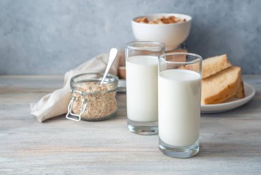 İki bardakta süt, gri arka planda ekmek ve yulaf ezmesi.