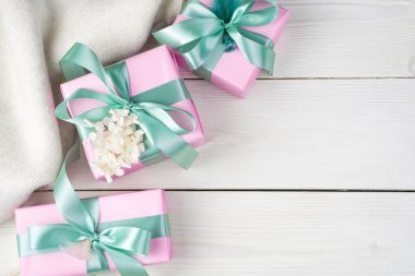 Kurdeleli pembe paketler ve beyaz ahşap arka planda bir süveter..