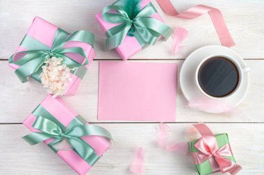 Hediyeler, kahve ve açık ahşap arka planda pembe tonlarda bir zarf içeren neşeli bir kompozisyon..