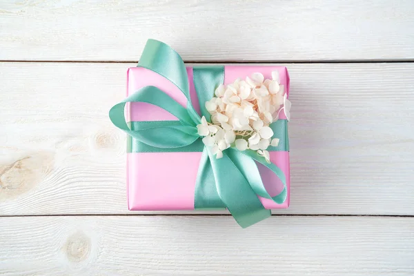 La caja de regalo rosa está decorada con una cinta y flores sobre un fondo de madera blanco. —  Fotos de Stock