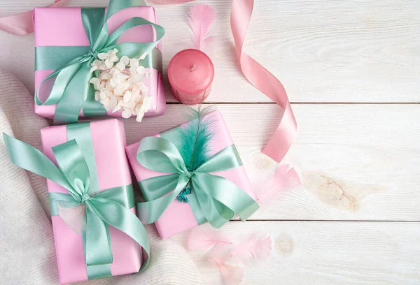 Tres cajas de regalo rosas, una vela y cintas sobre un fondo de madera blanco. —  Fotos de Stock