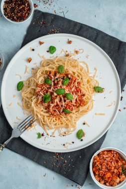 Düz tabakta domates ve fesleğen ile spagetti ve kalın et sosu, baharatlar ve gri arka planda koyu bir peçete..